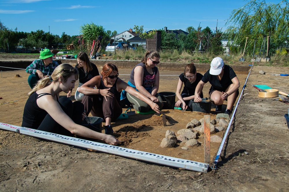 grupa osób zdejmująca warstwy ziemi z obiektu archeologicznego