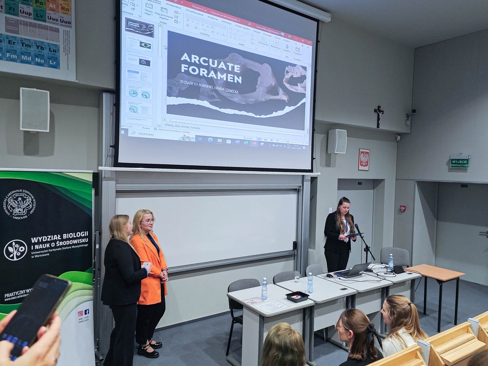 Prelegent przedstawiający prezentację w sali konferencyjnej, widoczny slajd tytułowy Arcuate Foramen