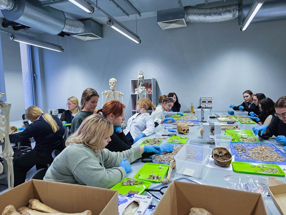 Grupa ludzi przy stole z tacami i pudłami ze szczątkami kostnymi
