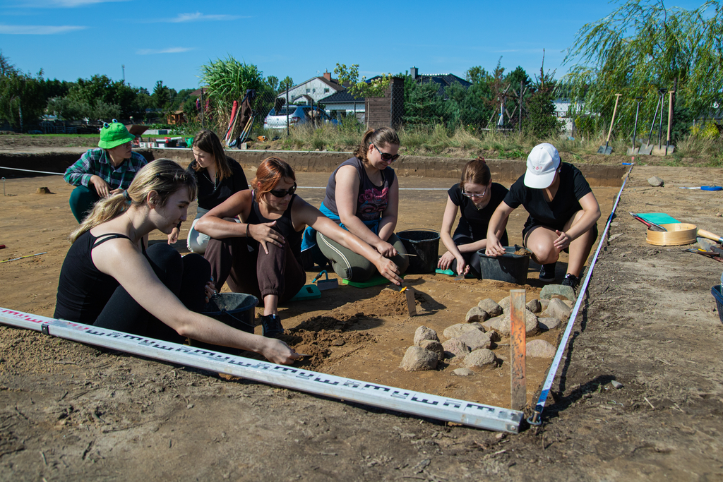 grupa osób zdejmująca warstwy ziemi z obiektu archeologicznego